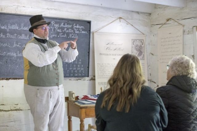 A man with a jaunty hat and period attire is visually telling a story to onlookers 