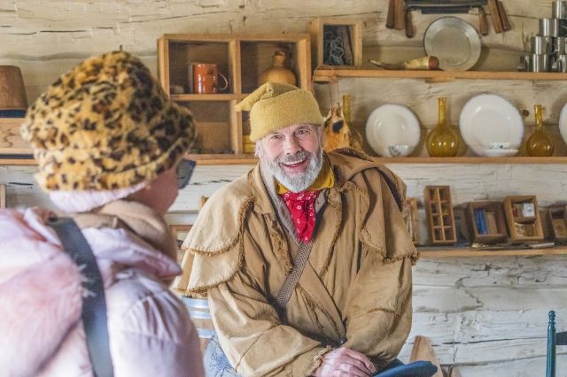 A jolly man in period attire talks with a lady in a jaunty leopard fur bucket hat