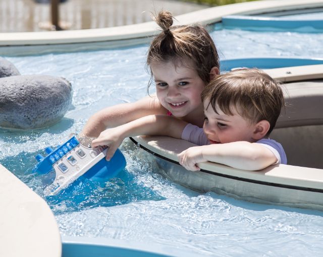 kiddos with a toy boat playing in a river simulation at the splash pad