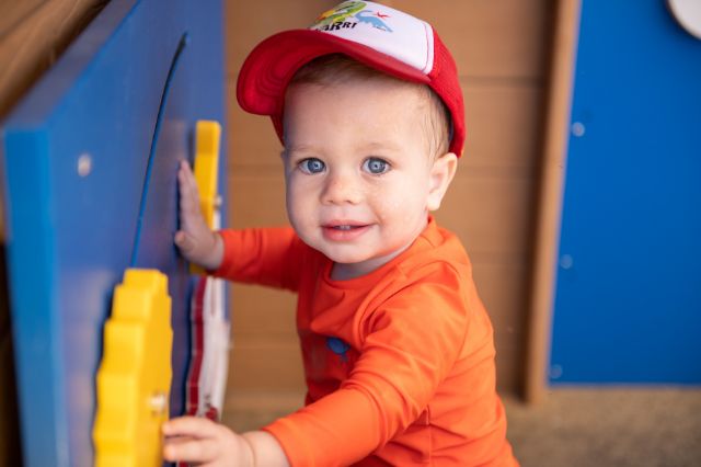 little guy with a hat on playing with toy gears mounted to a wall