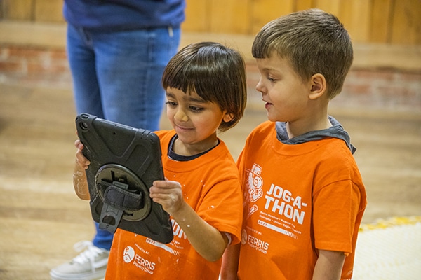 Two young boys learning from and ipad wearing Jog-a-thon shirts so fly