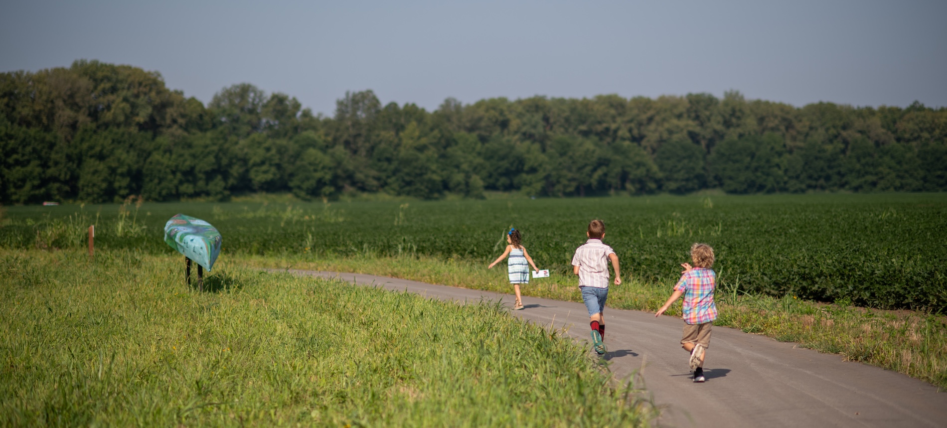 Kids running down a trail through a field. One kid is wearing a canoe like a turtleshell and he appears to be winning the race.